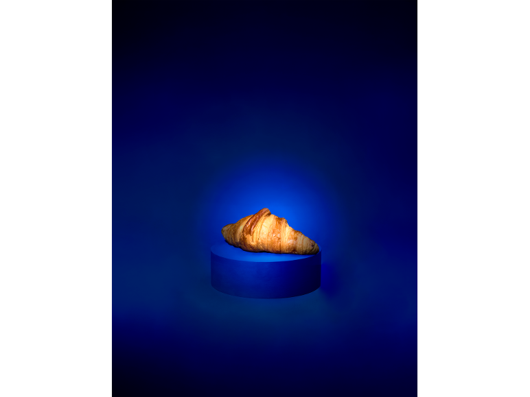 A golden croissant on a blue pedestal against a dark blue background.