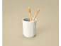 Two bamboo toothbrushes in a white ceramic cup on a beige background.