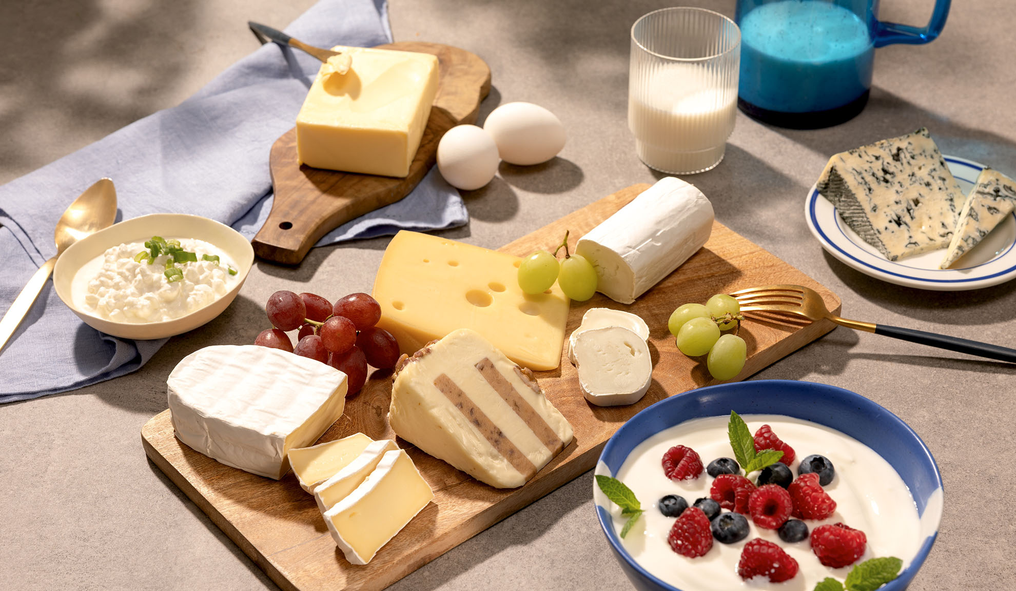 A variety of cheeses, grapes, and dairy products like cottage cheese, milk, and yogurt with berries.