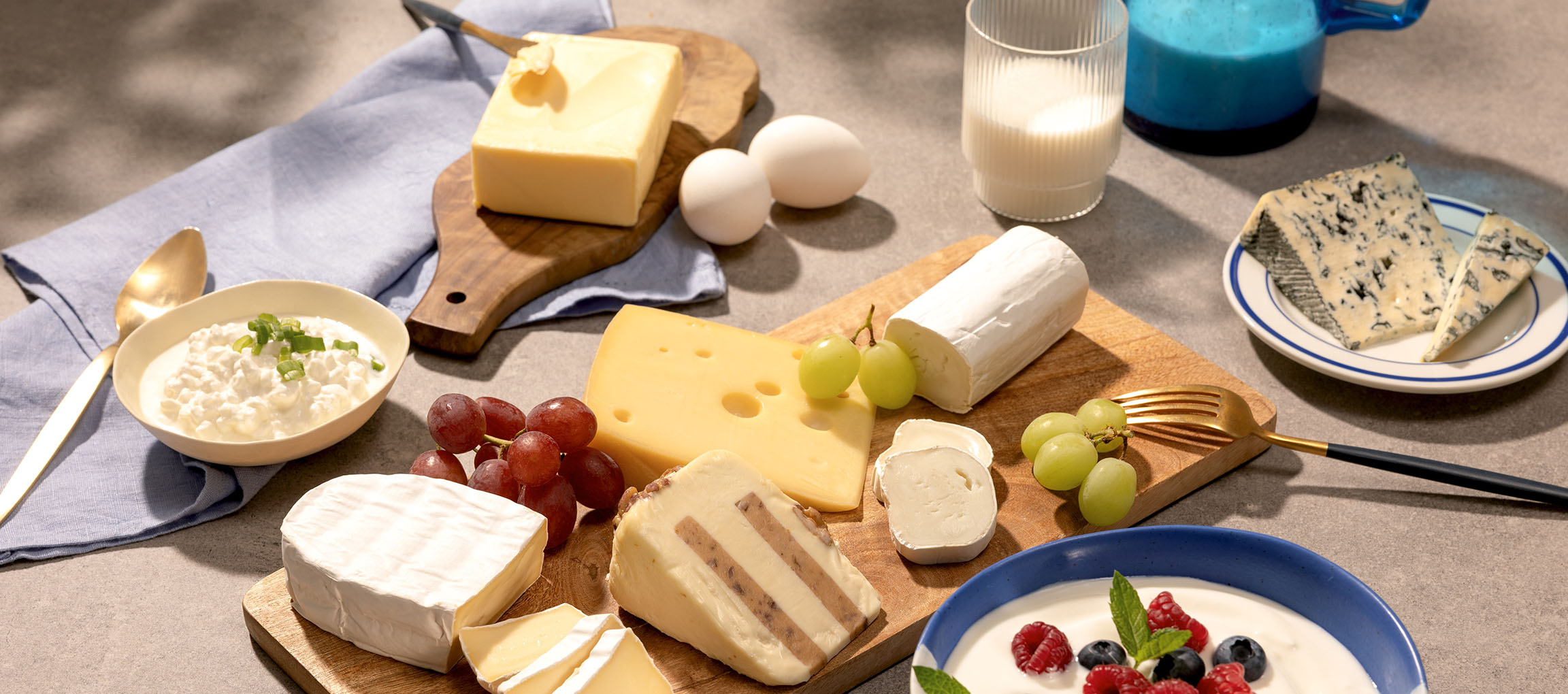 Assortment of cheeses, eggs, grapes, milk, and yogurt with berries on a table.
