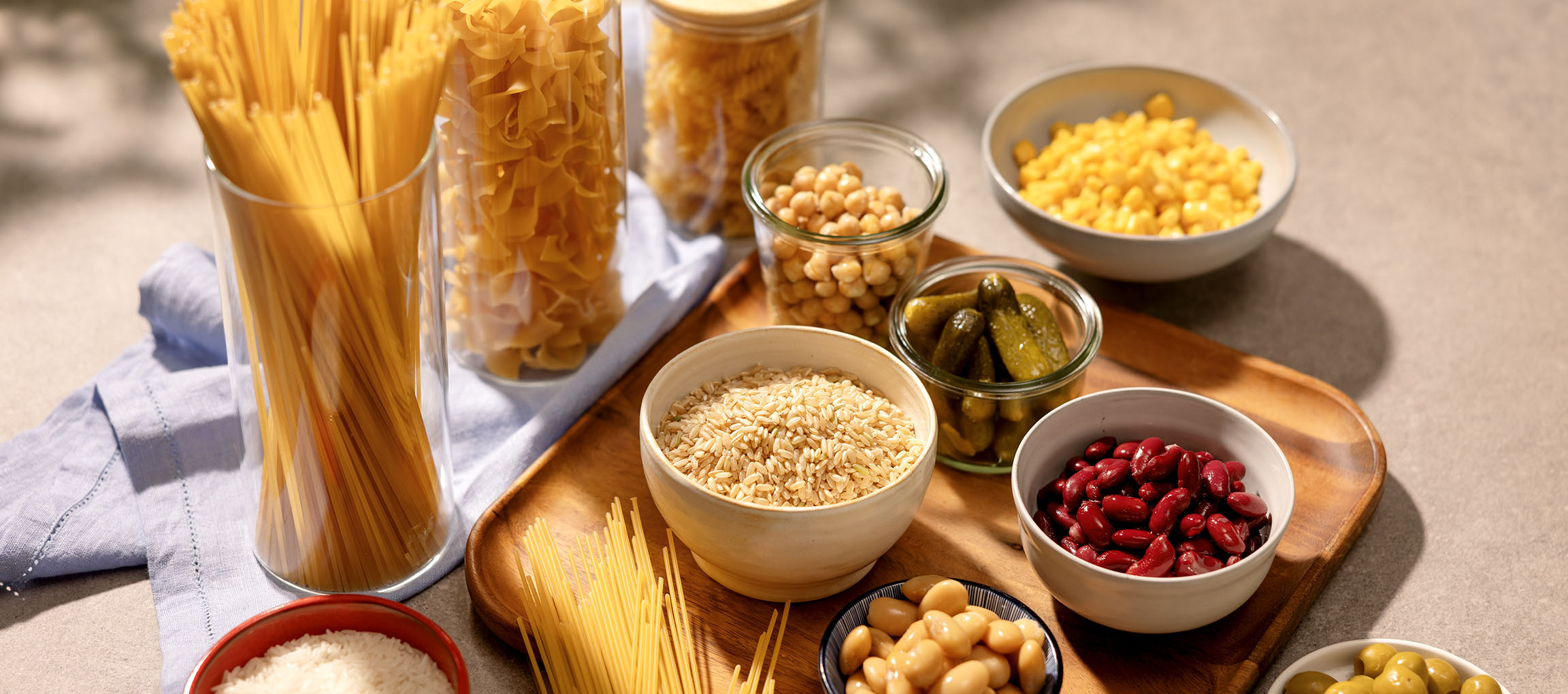 Various dry goods and canned vegetables: pasta, rice, chickpeas, corn, beans, pickles.