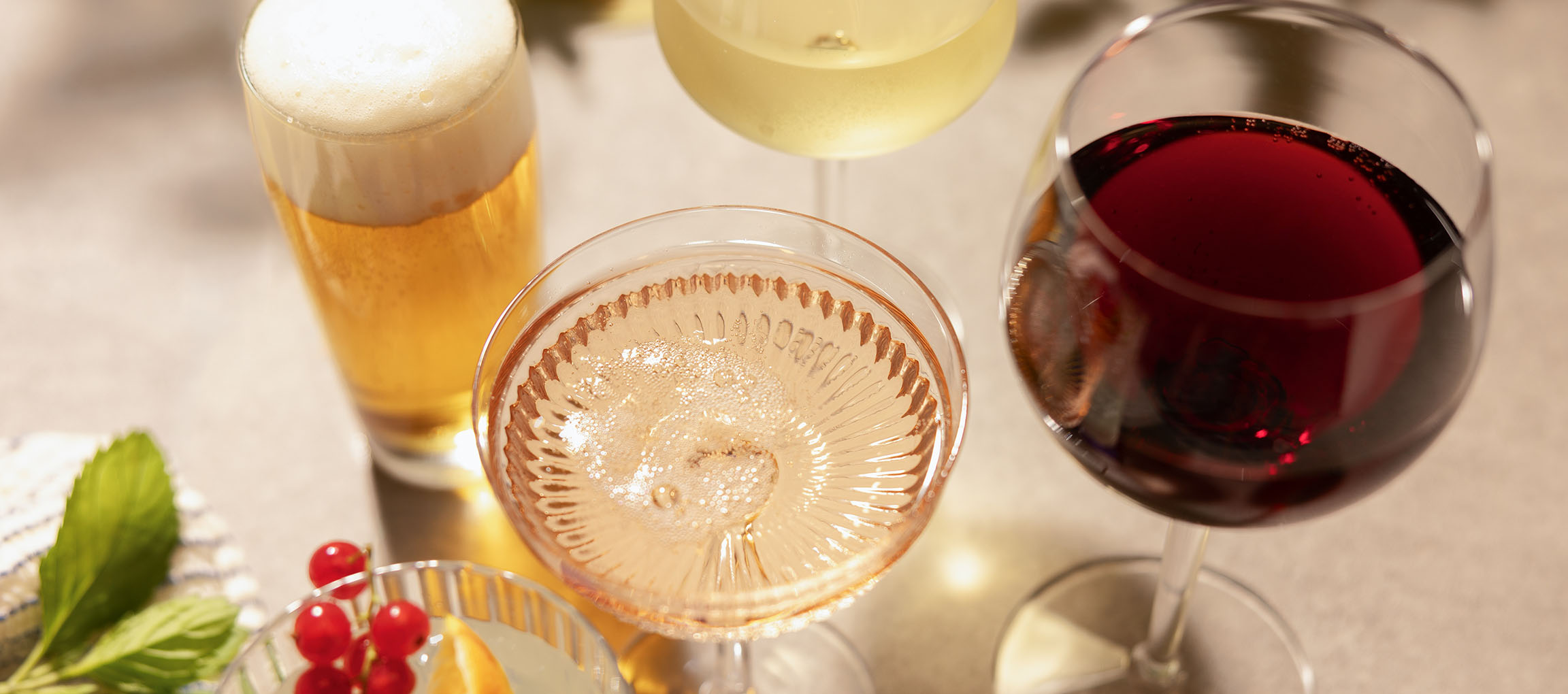 Beer, rosé wine, and red wine in glasses, with berries and mint.