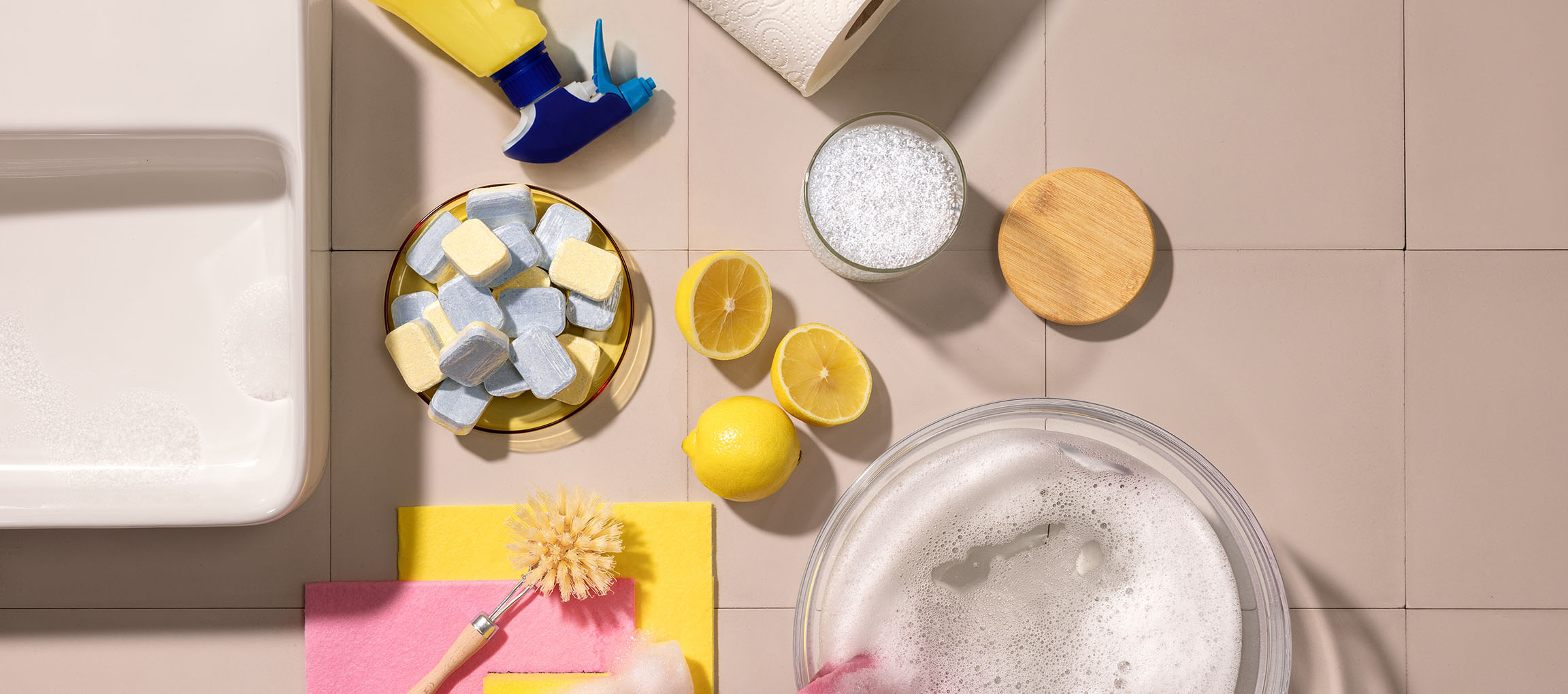 Cleaning supplies: dishwashing tablets, lemons, spray bottle, paper towel, brush, sponges.