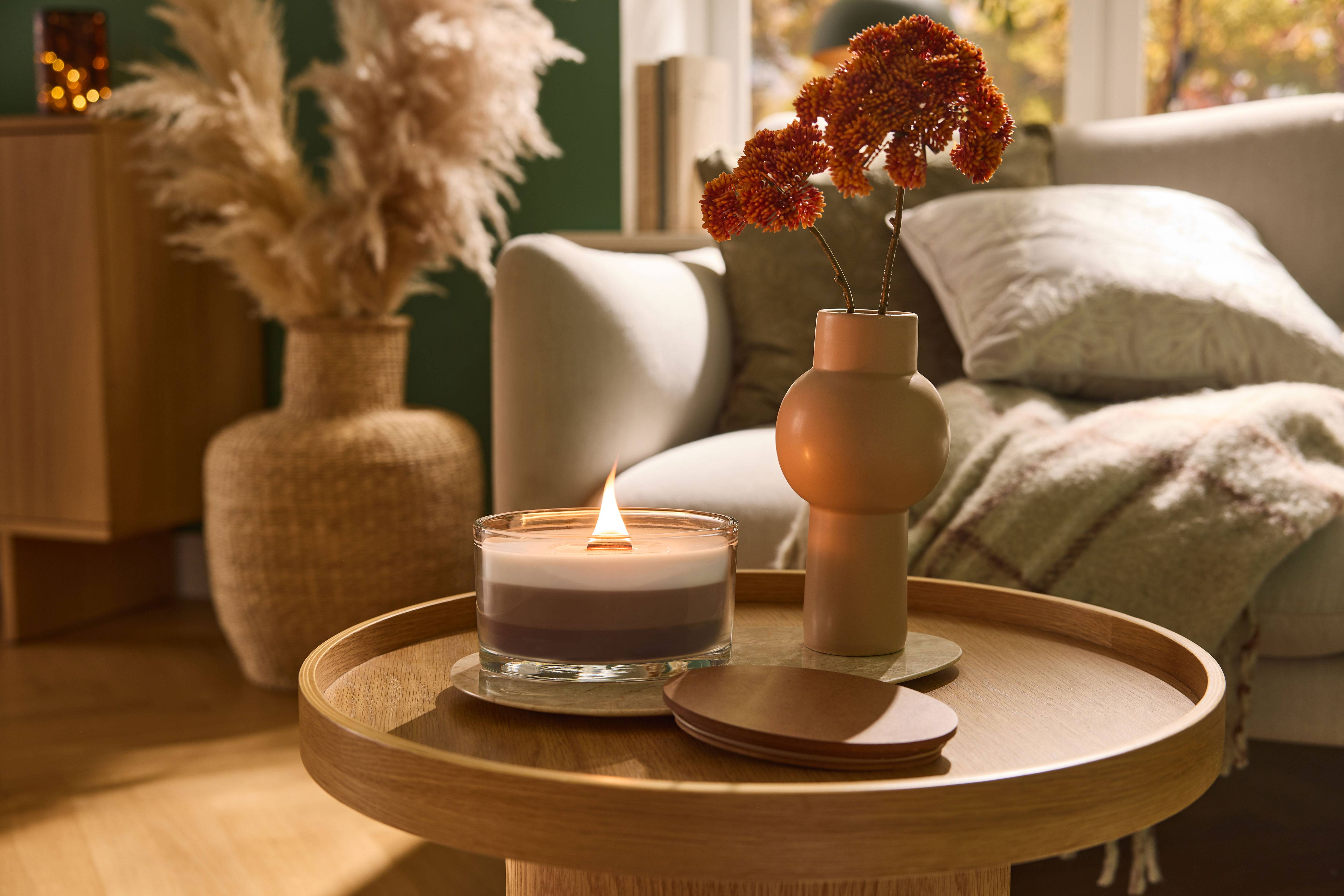 Burning candle and vase with flowers on a wooden coffee table in a living room.