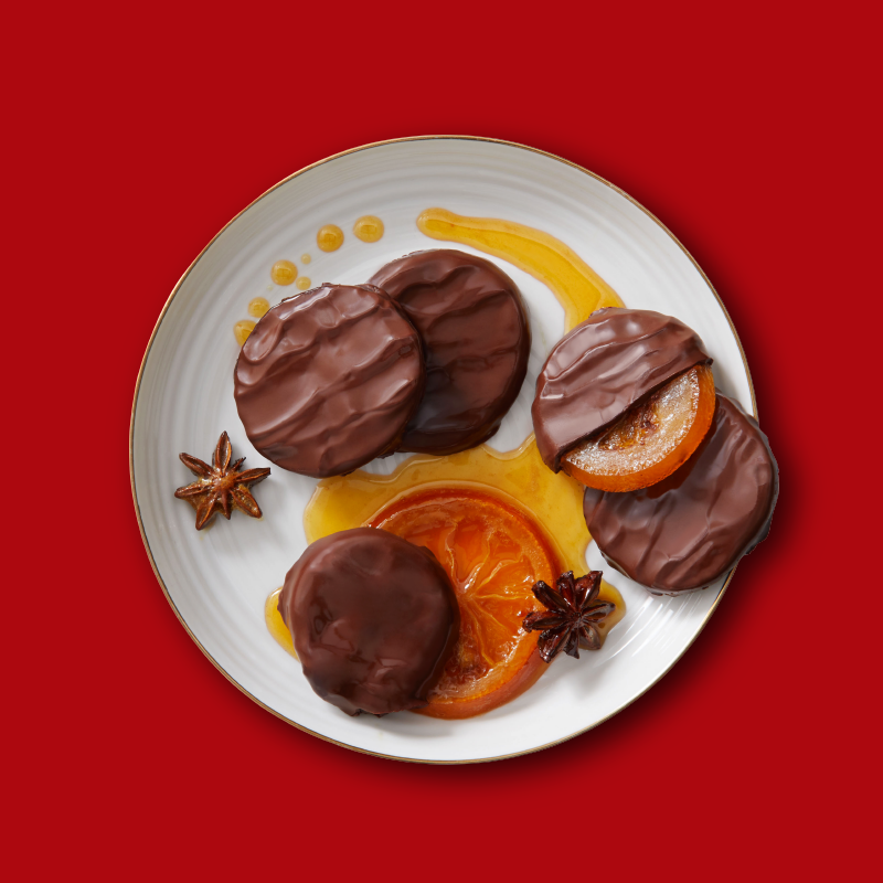Chocolate-covered candied orange slices and cookies with honey and star anise on a white plate.