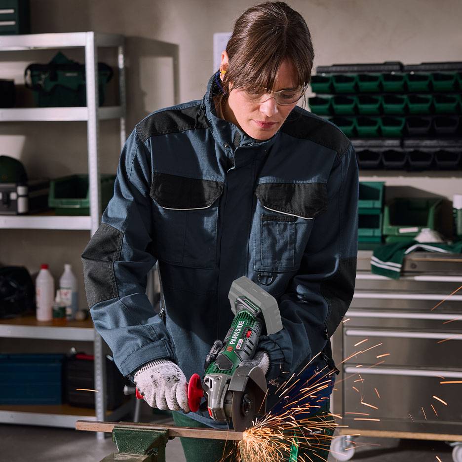 Woman with angle grinder cutting metal, with sparks, in a workshop setting.