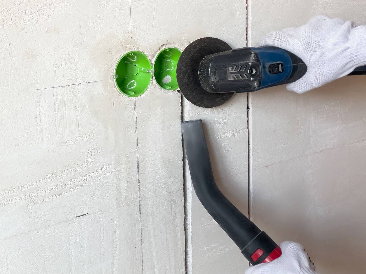 Power tool cutting grooves into a wall with a vacuum cleaner for dust.