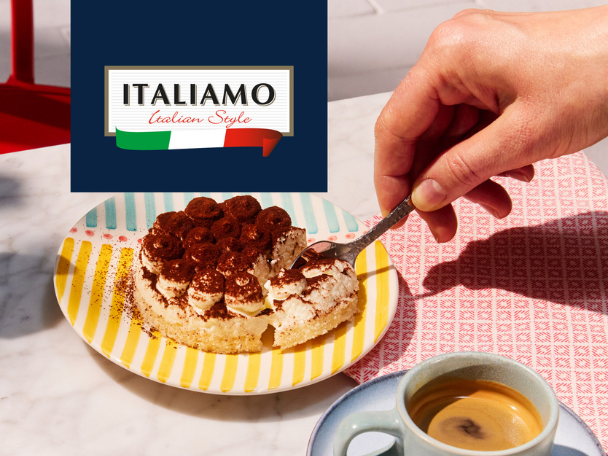 A hand spoons a bite of tiramisu from a colorful plate next to a cup of espresso.