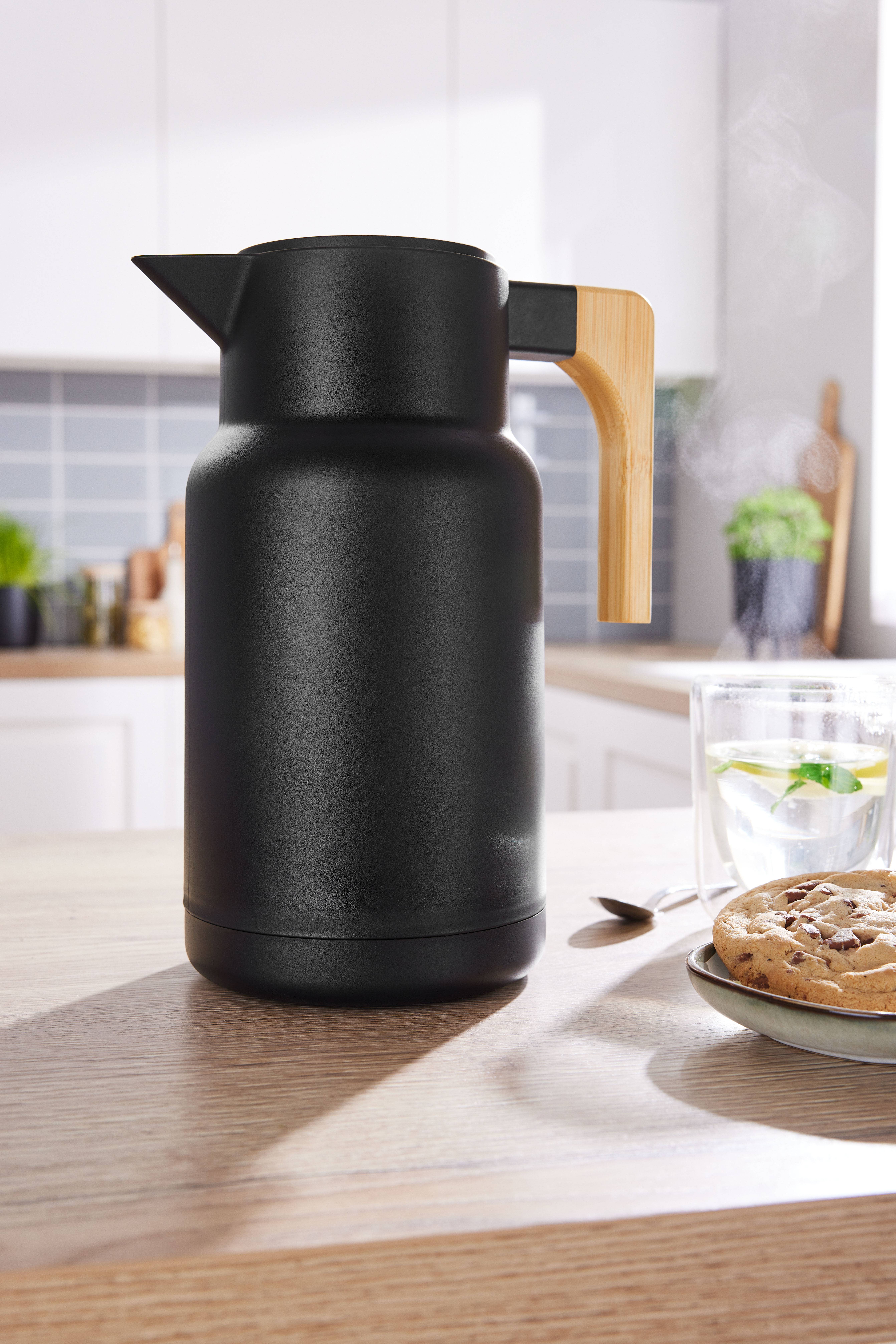 Black thermos with a wooden handle on a kitchen table with cookies and tea.