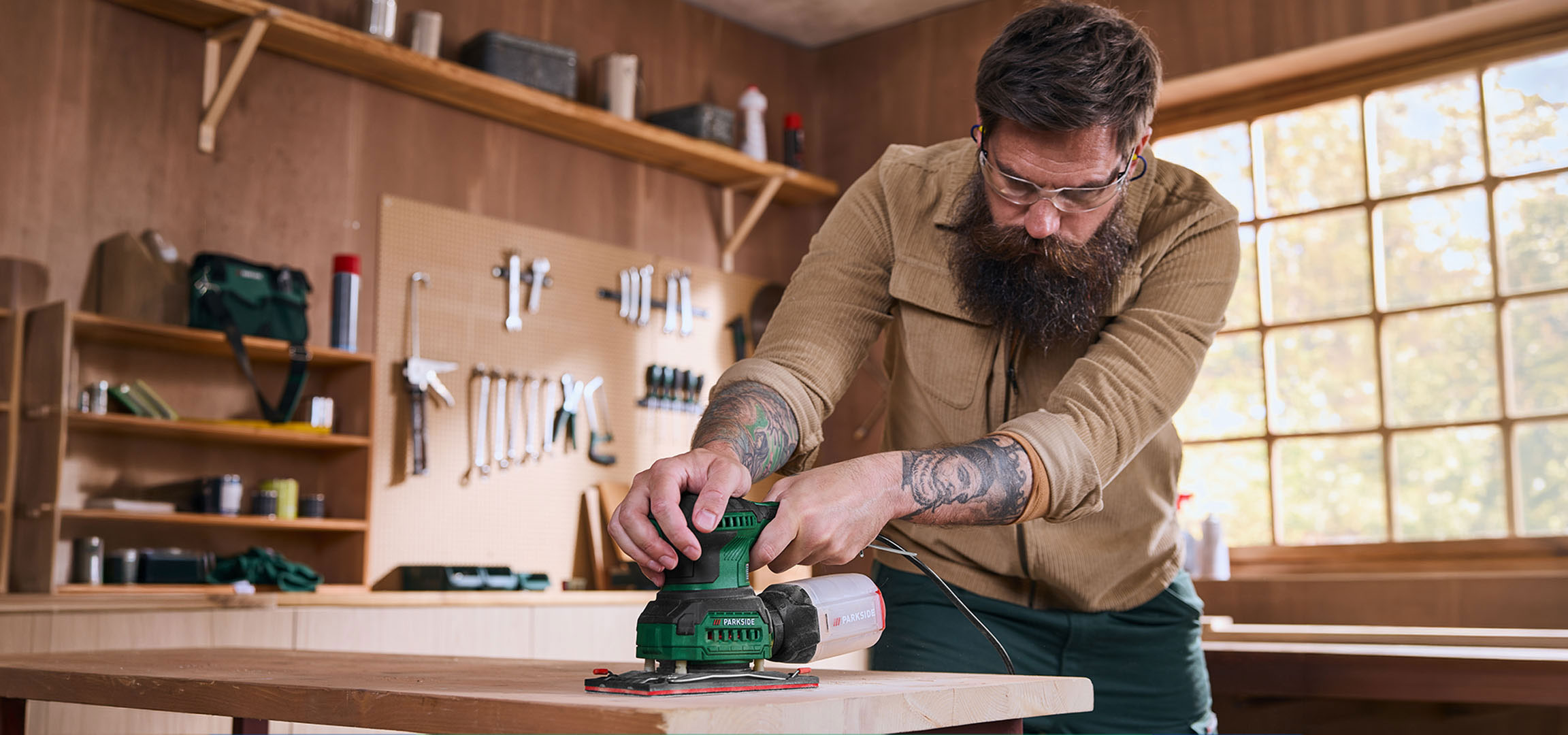 aiLabeling.aiLabelForImageAltText: Man with electric sander sanding a wooden table in a workshop.