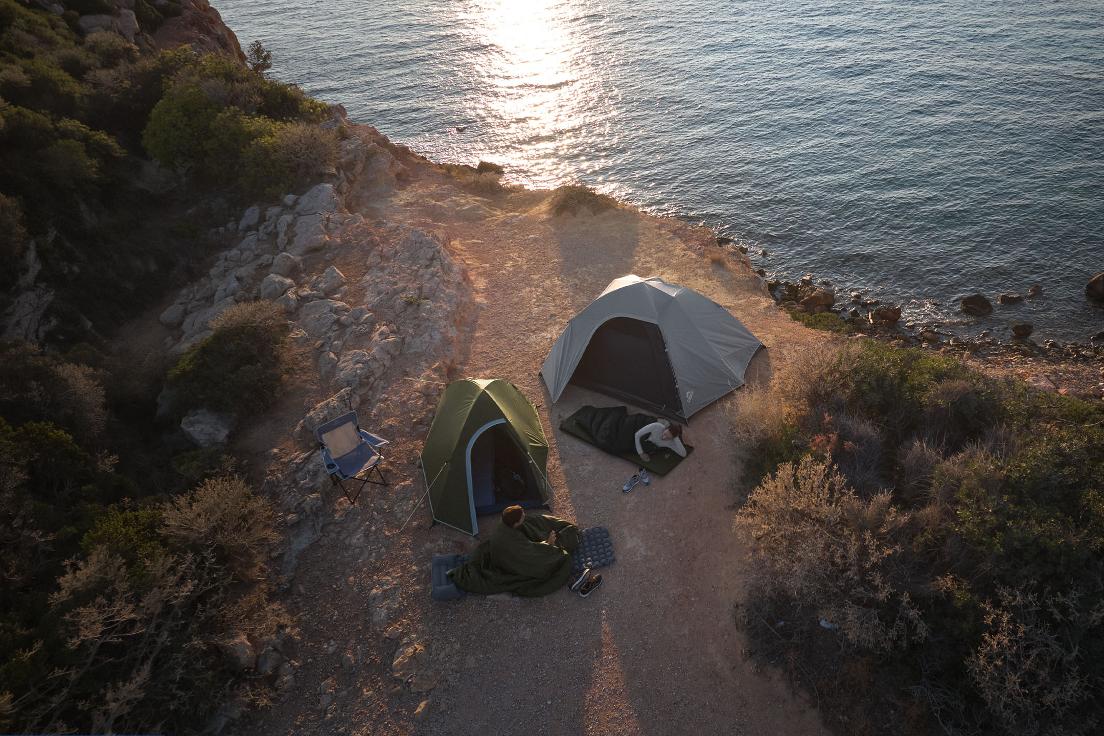Two people camping in tents on a rocky coast, with a sea view.
