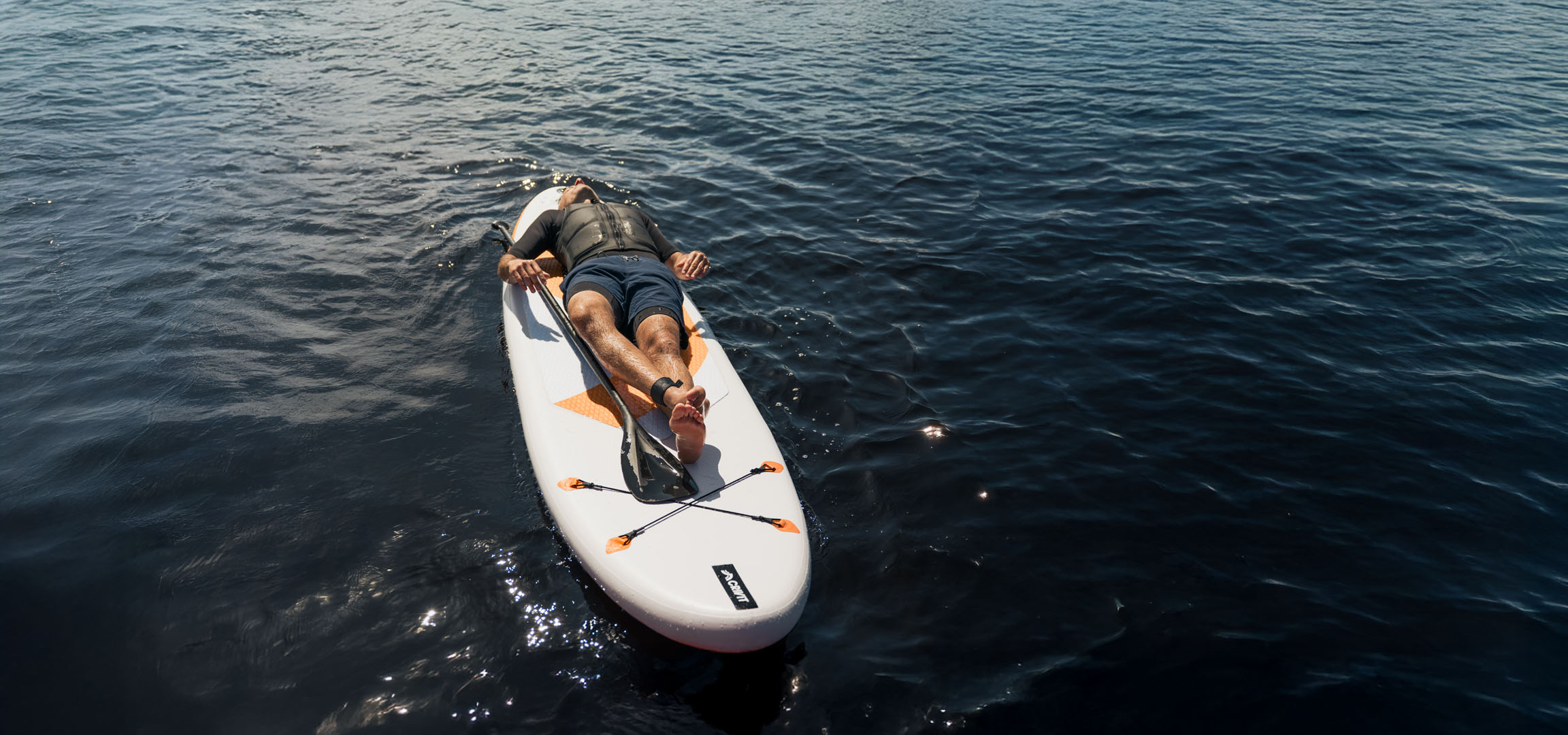Homem relaxando em uma prancha de stand-up paddle em água calma.
