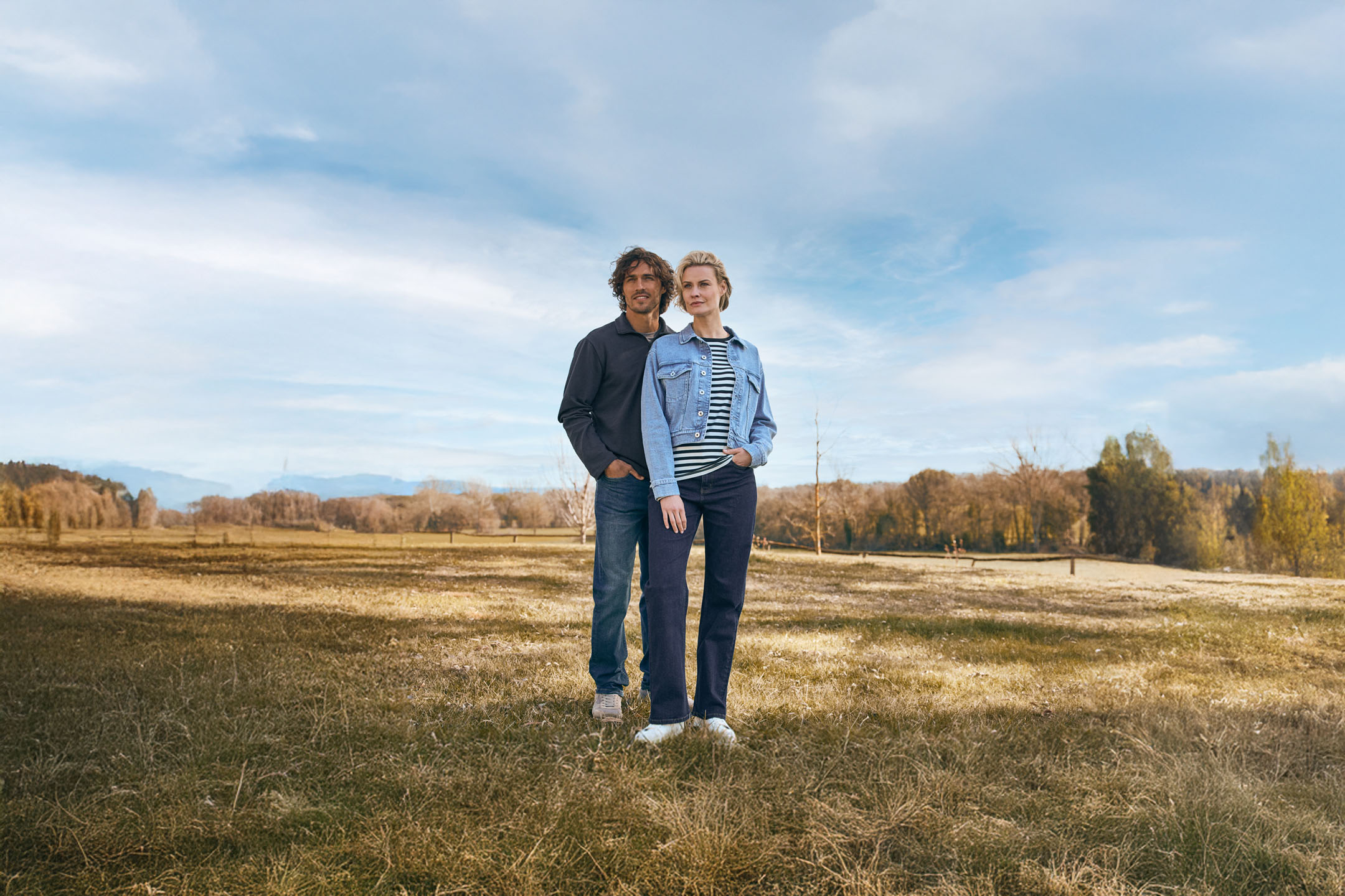 Casal com jaquetas jeans em ambiente rural.
