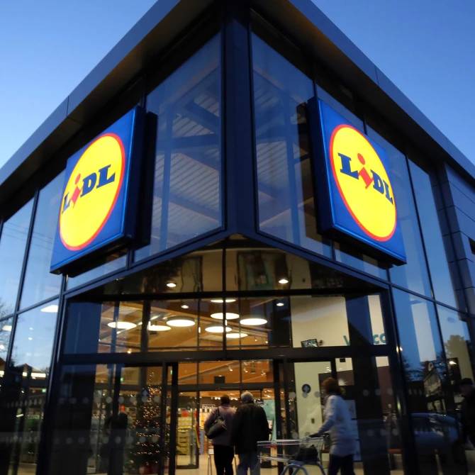 Exterior of a modern Lidl store with large glass windows and illuminated signs.